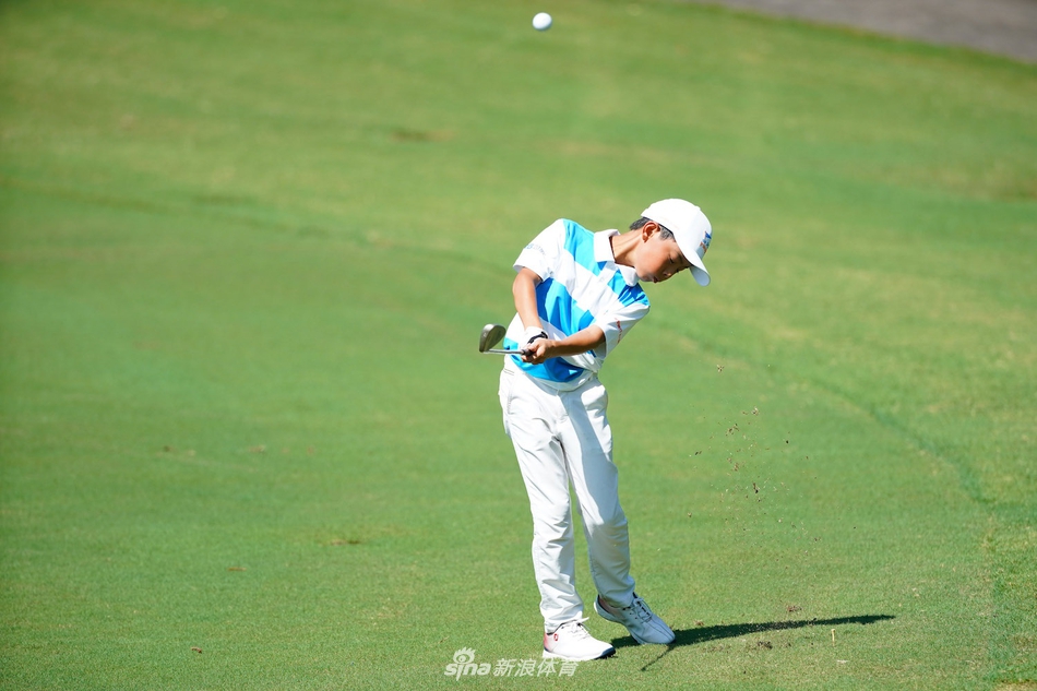 小球员在果岭边细致观察线路，他蹲下身，目光如炬，认真研判着草纹的走向与坡度。