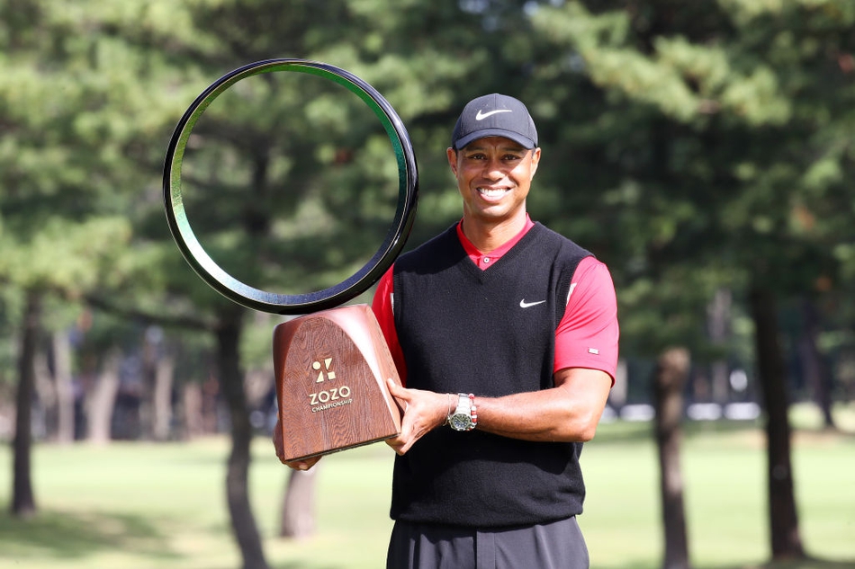 伍兹高高举起ZOZO锦标赛冠军奖杯，笑容灿烂，身后是漫天飞舞的彩带与欢呼的观众。