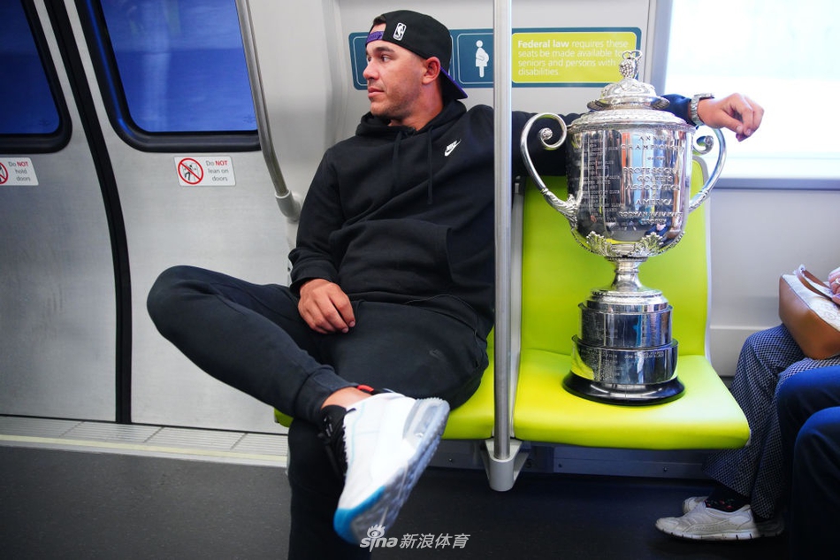 科普卡身着休闲装，手捧银光闪闪的沃纳梅克奖杯，微笑着站在地铁车厢门口，仿佛一位凯旋的都市骑士