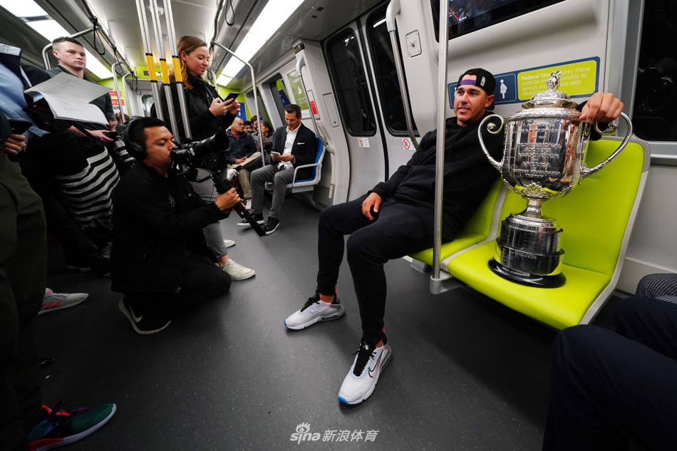 科普卡低头凝视怀中的奖杯，地铁车窗映出他专注的侧脸与流动的城市光影，画面充满故事感