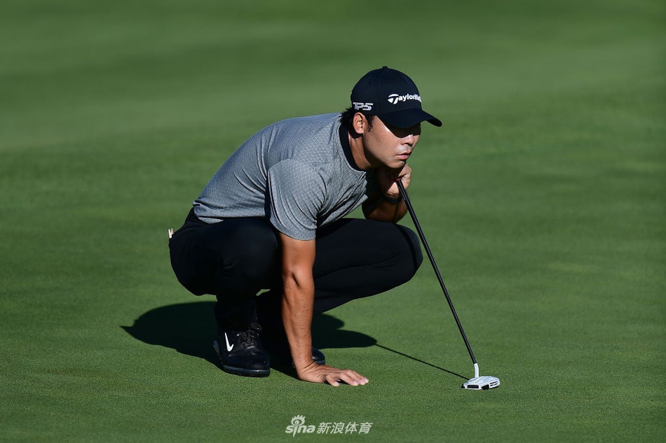 张新军在第十二洞果岭边凝神观察，身后是宽阔的水障碍与明尼苏达湛蓝的天空，他刚刚在这里推进关键老鹰推，取得了梦幻开局