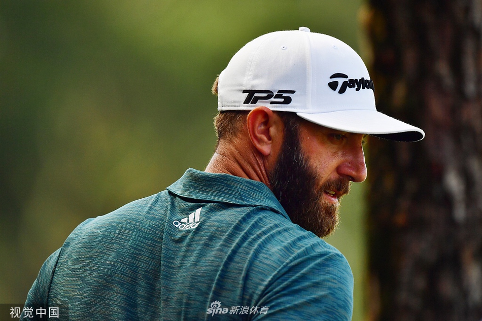 达斯汀-约翰逊在发球台上全力挥杆，身体充分扭转，力量感瞬间爆发，白色高尔夫球在蓝天背景下划出优美弧线。