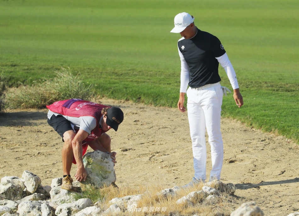 李昊桐半蹲在果岭边长草中，手持推杆仔细研判草纹与坡度，眼神专注。