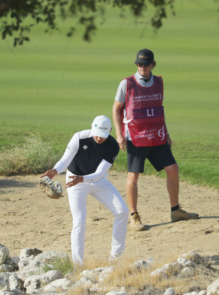 李昊桐站在发球台上眺望远方球道，强风吹拂着他的衣角和短发，表情凝重而坚定。