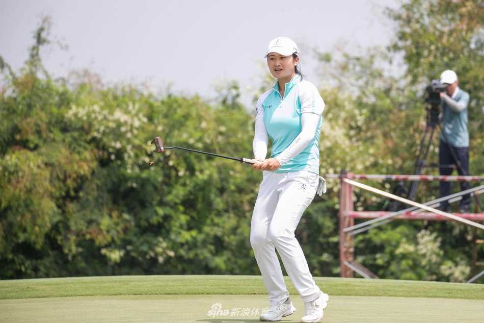 比赛中的殷若宁与球童认真讨论策略，手指远方果岭，专注的神情体现着高尔夫运动的智慧与谋略。