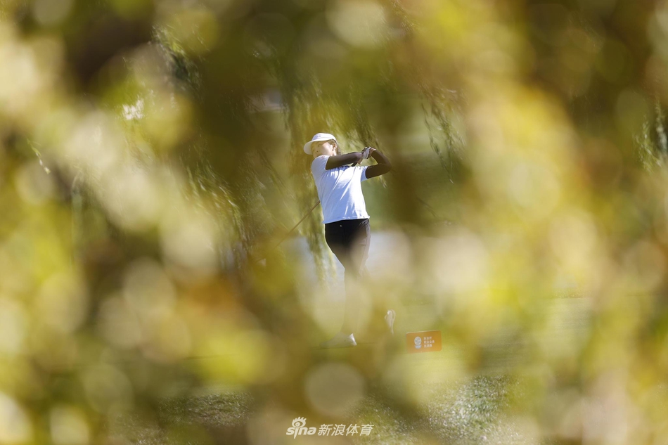 肖博文在发球台奋力开球，身体扭转充满力量，白色的高尔夫球在空中飞向远方，背景是连绵的球道。