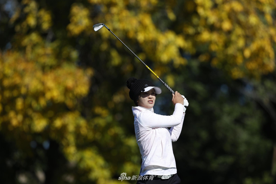 高尔夫球手张维维在果岭边躬身仔细研判推杆路线，神情专注，背景是广阔的球场与蔚蓝的天空。