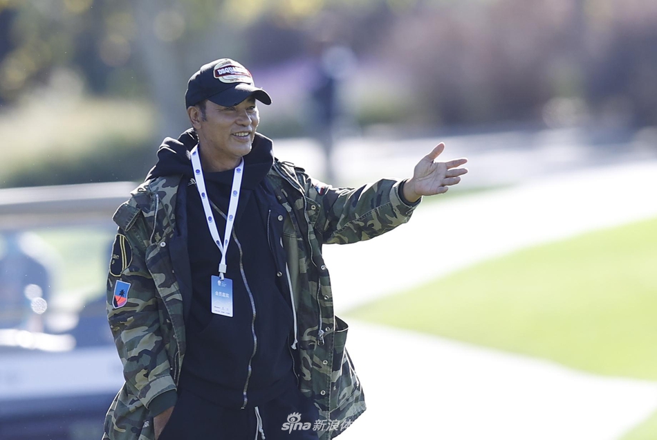 影视明星任达华戴着墨镜，神情专注地站在球场边观看比赛，阳光洒在他的侧脸，展现出沉稳的明星风采。