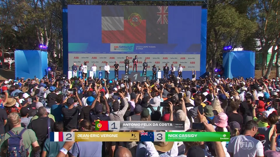 远景车队赛车驶过开普敦地标背景的赛道，远处桌山的平顶与城市的现代化建筑在速度的映衬下显得格外壮丽。