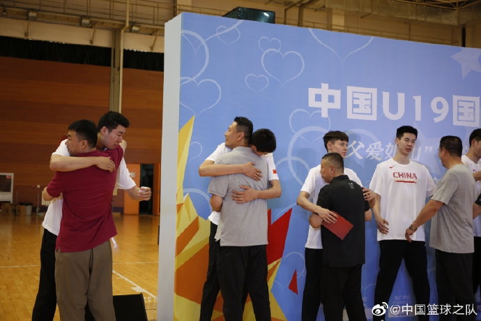 在摆满篮球的签名区，一名国青球员单膝跪地，认真地在印有自己号码的展板上签名，身后是队友们充满青春气息的身影。