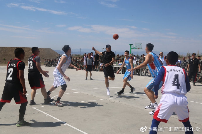 球员们走进部队宿舍参观内务，一名战士正在展示如何叠出标准的“豆腐块”被子，球员们看得入神，纷纷竖起大拇指称赞。