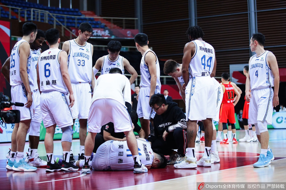 队医蹲在地上紧急查看吴冠希的伤情，用手轻轻触碰他的左脚踝进行初步诊断，吴冠希则用手臂遮住双眼，难掩失望与痛苦。