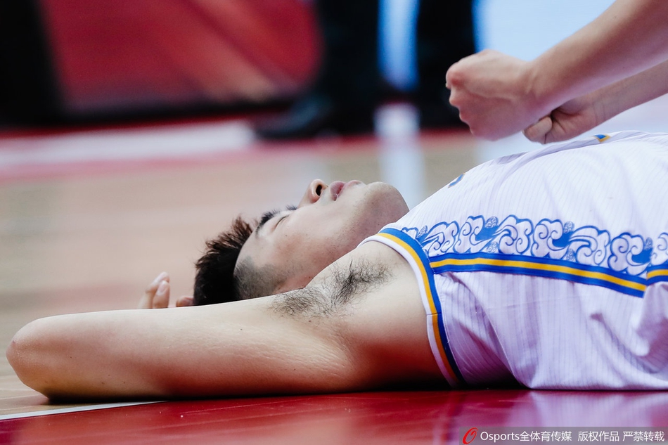 吴冠希痛苦倒地，双手紧紧捂住左脚踝，面部表情因剧烈的疼痛而扭曲，队友们神色焦急地围在身边。