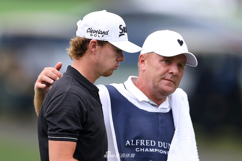 赛事全景，绿茵如毯的球场与远山蓝天构成壮丽背景，选手正在果岭上观察线路