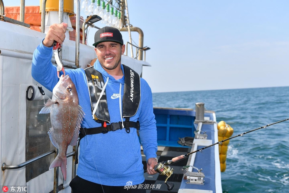 科普卡手持新鲜钓获的海鱼展露笑颜，身后济州岛的碧海晴空与他的喜悦神情相映成趣
