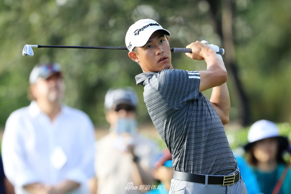 科林-森川面带微笑走向下一个发球台，充满自信，周围是郁郁葱葱的热带植物与驻足观看的球迷