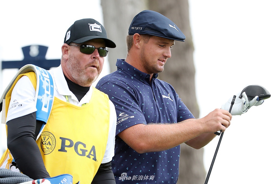 德尚博与球童讨论战术，表情专注，仿佛正在重新计算失去一号木后的球场攻略