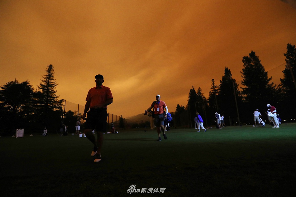 一名高尔夫球手在练习果岭上推杆，他的身影与背后被山火染成一片橙红色的天空形成鲜明对比，如同在另一个星球上竞技。