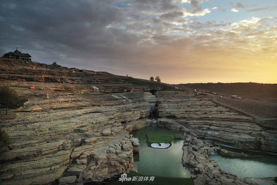 蜿蜒的球道如丝带般穿过天然草场与石灰岩地貌，沙坑的线条与远山的轮廓和谐相融。