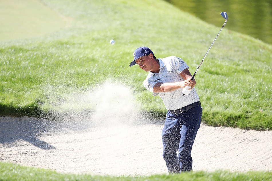 里奇·福勒身着橙色上衣在黄昏的球道上行走，成为沙漠景观中一抹亮丽的风景线，姿态轻松而自信。