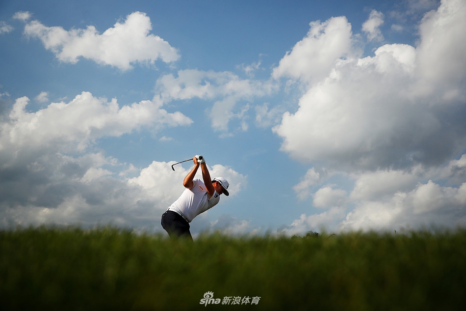 中国球员张新军在全神贯注地推击，帽檐下的眼神坚定，身旁广阔的球场是他国际赛场上奋斗的舞台。