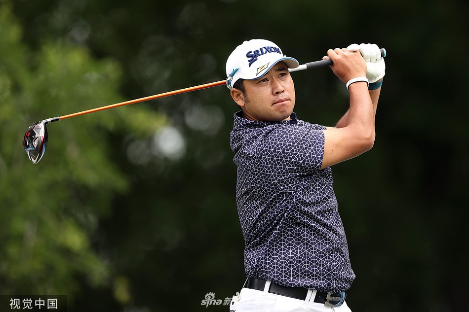 松山英树在绿意盎然的球道上漫步前行，神情平静，正在比赛中稳步推进。