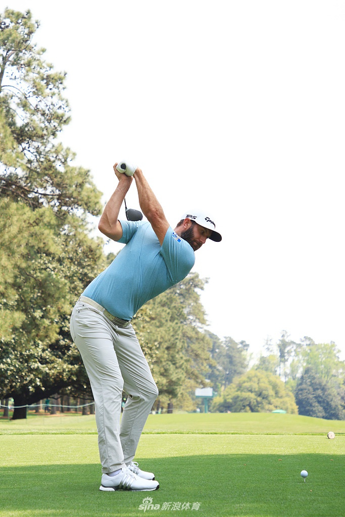 达斯汀·约翰逊在球道上轻松挥杆，动作流畅充满力量，背景是奥古斯塔葱郁的松树