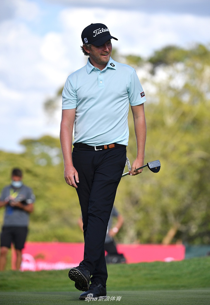 哈丁面带沉稳微笑，手捧肯尼亚公开赛冠军奖杯，奖杯在阳光下熠熠生辉，周围绿意盎然。