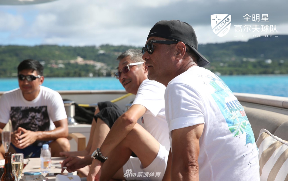 球队成员在游艇甲板上轻松交流,背景是塞班岛苍翠的山峦与辽阔海洋