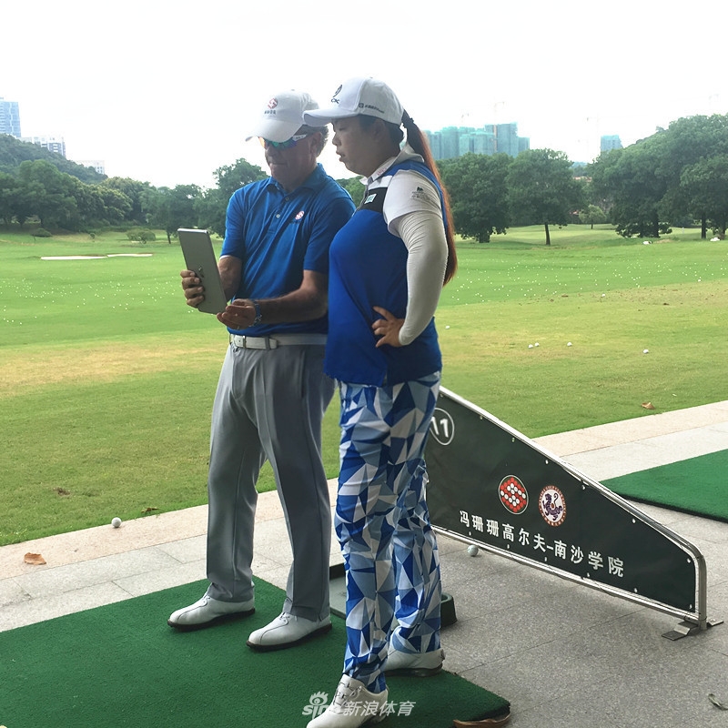 冯珊珊站在练习场边，目光温柔地注视着远处一位正在全力挥杆的小球员，眼神中充满了鼓励与期许。