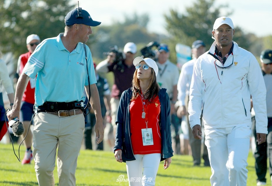 赫尔曼面带微笑走在伍兹前方,伍兹则紧随其后,背景是开阔的高尔夫球场与观众