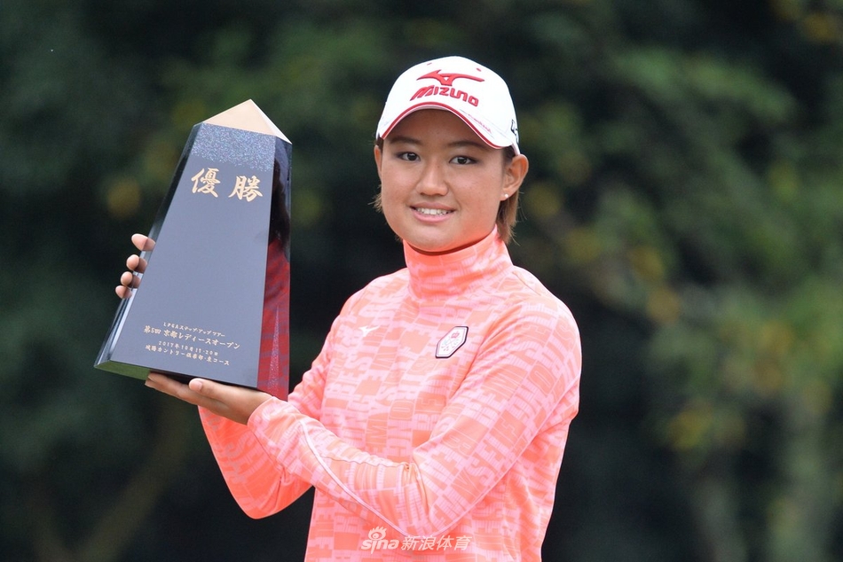 冠军选手高举奖杯瞬间，灿烂笑容与银色奖杯在阳光下交相辉映，身后是鼓掌的观众