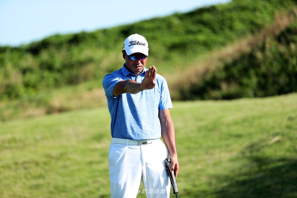 中国高尔夫球手王煦在果岭边屈膝，全神贯注地观察推杆线路，展现出职业球员在比赛关键时刻的细致与专注。