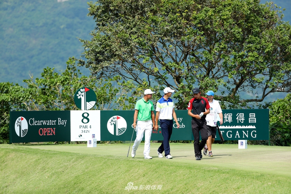 金诚与同组球员在开球前于发球台合影，三人手持球帽神情愉悦，身后的清水湾球场海天一体景色壮丽