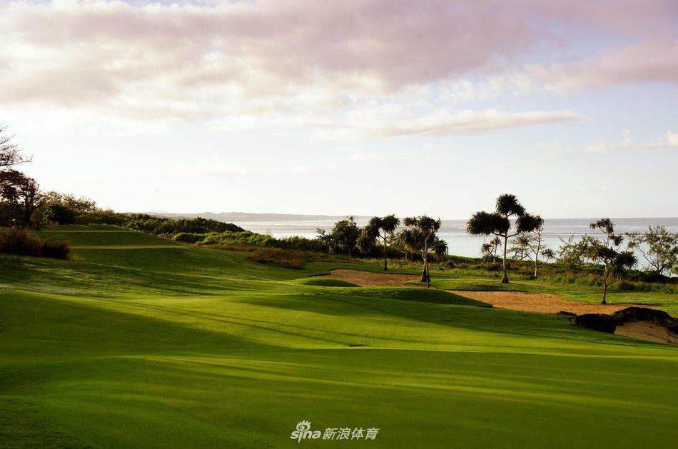 夕阳下的球场全景,球道如绿丝带蜿蜒在珊瑚海岸与深蓝海洋之间
