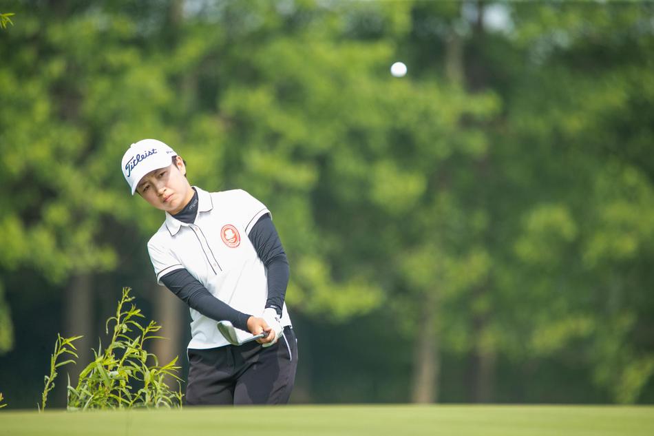 中国球员杨嘉欣优雅挥杆,身姿舒展,白色的运动上衣与绿草茵茵的球场相映成趣。