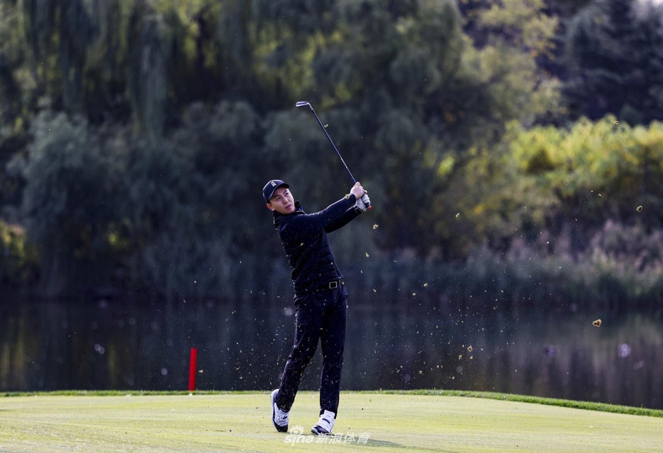 张哲瀚站在果岭上准备推杆，他双手握杆，身体形成完美的角度，阳光洒在他身上，在绿茵地上投下充满力量感的剪影。