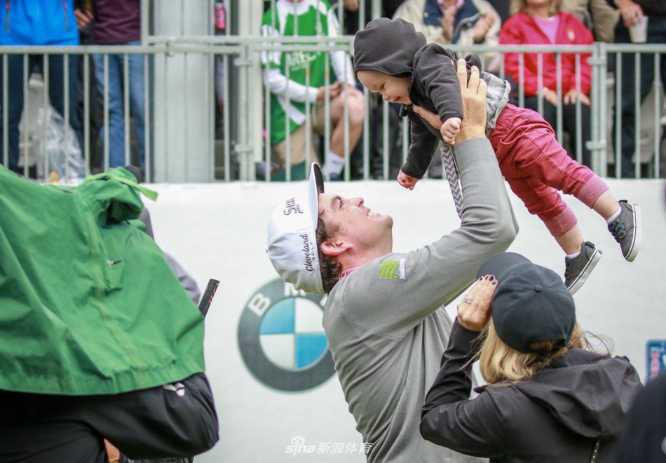 布拉德利兴奋地将年幼的儿子高高举过头顶，孩子开心地笑着，父亲脸上满是自豪，背景是绿茵赛场，象征着胜利的喜悦与生命的传承在此刻交汇。