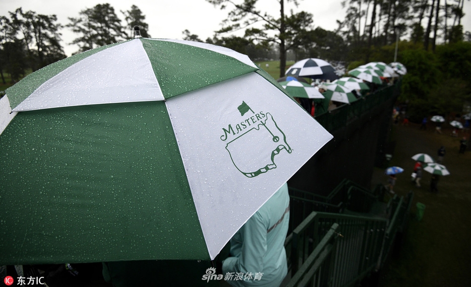 雨丝如银线般掠过镜头，前景中一把撑开的透明雨伞上挂满晶莹水珠，伞后是奥古斯塔闻名遐迩的会所和郁郁葱葱的树木，宛如一幅印象派油画。