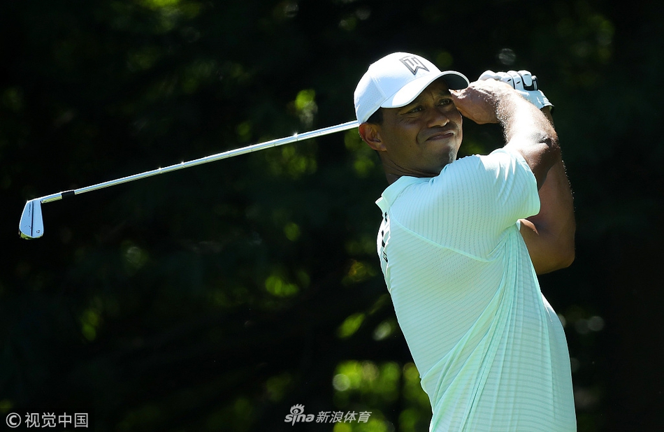 比赛现场广阔的球道视野，可以看到球员与球童走在修剪整齐的草坪上，远处是浓密的树林。