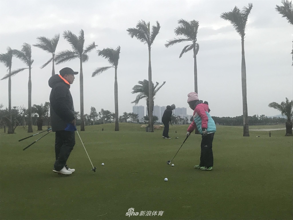 刘宇婕在练习推杆,父亲刘国梁站在一旁专注观看,温暖的夕阳将父女二人的影子拉长在果岭上