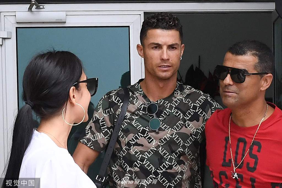 熙攘的人群中，C罗微微侧身倾听球迷话语，乔治娜在其身后静静注视，阳光透过人群缝隙洒在他们身上，构成一幅偶像与爱同行、与民同乐的温暖画面。