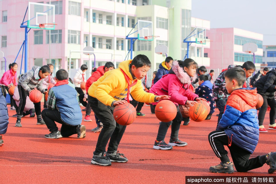 宽阔的操场上，孩子们在老师的带领下变换着队形，运球奔跑。红蓝相间的校服与绿色的草坪相映成趣，整个校园都沉浸在运动的欢乐海洋中。