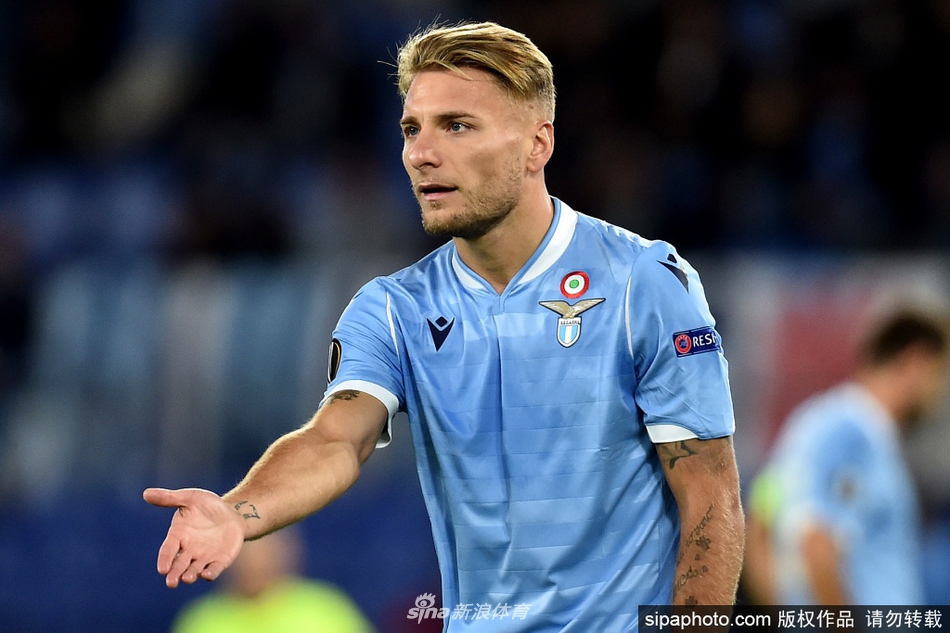 训练场上，因莫比莱面带专注而平和的微笑，与队友们轻松交谈，身后是湛蓝的天空和绿茵场，展现出他作为球队领袖平易近人又充满凝聚力的一面