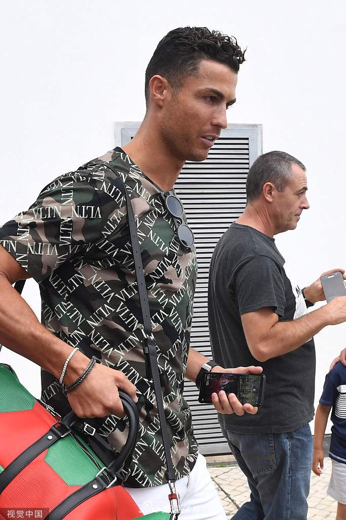 C罗一手轻扶球迷肩膀，一手执笔签名，专注的神情仿佛在完成一件艺术品，乔治娜手持饮品在不远处温柔注视，定格了旅途中最自然的陪伴瞬间。