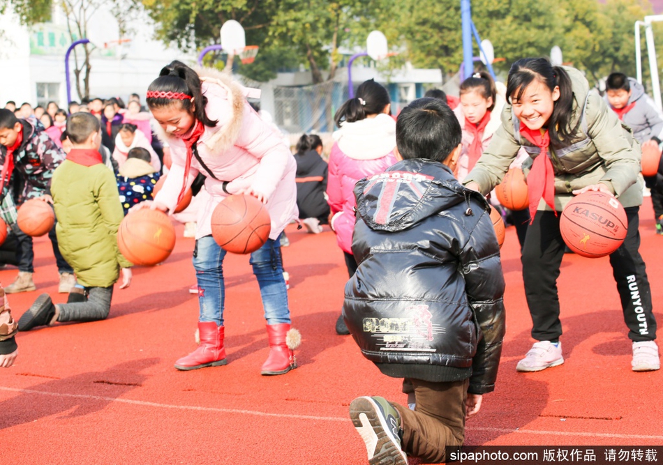 一名小学生正在做胯下运球，动作虽然还不太熟练，但紧抿的小嘴和坚定的眼神透露出不服输的劲儿，阳光下他小小的身影充满了运动的力量感。