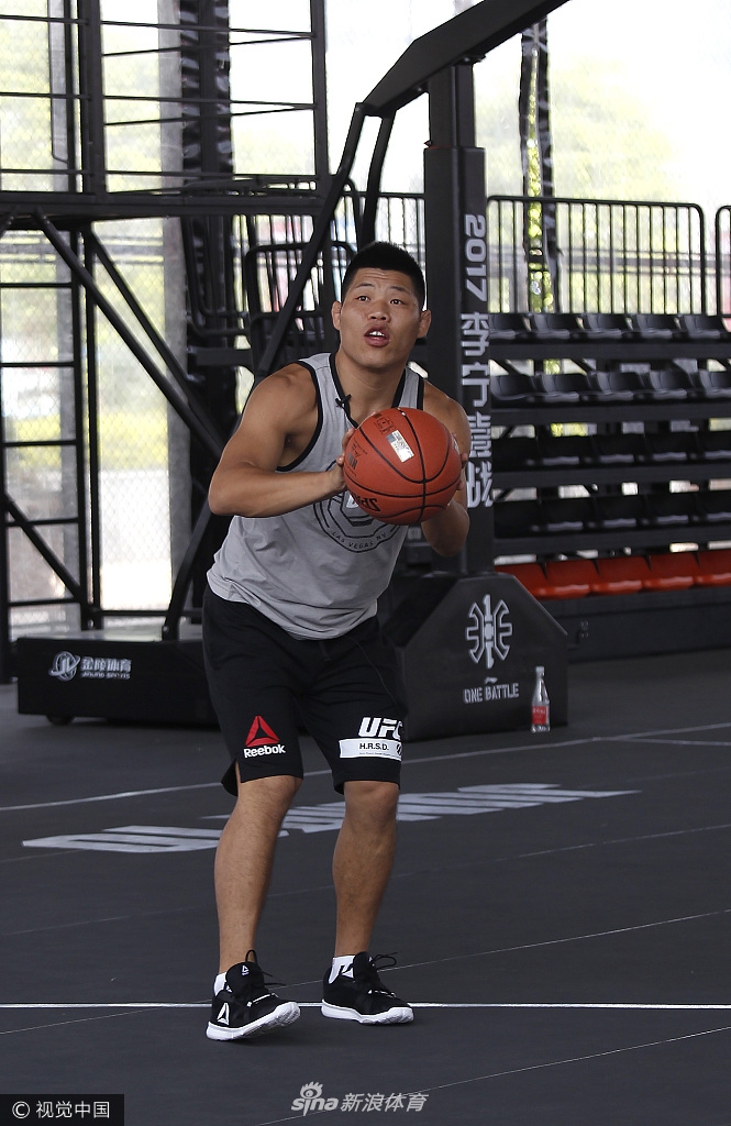 霍洛威双手运着两个篮球，脸上洋溢着搞怪的笑容，他似乎在向身边的篮球手们炫耀自己的控球技巧，轻松诙谐的氛围感染了在场的每一个人。