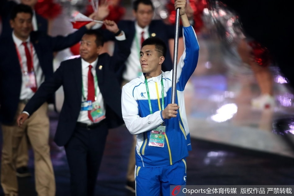 聚光灯下的郭艾伦，身姿挺拔，面带微笑，挥舞旗帜的动作潇洒而有力。