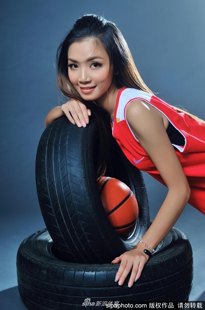 钟苑庄坐在篮球上,双腿自然前伸,明媚笑容与球场木地板的暖色调相得益彰