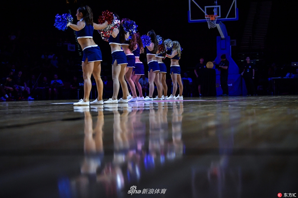 两位啦啦宝贝近距离特写，她们额头微微出汗，却依然保持着标准的露齿笑容。身后的篮球架和看台虚化为背景，更凸显了她们作为赛场焦点的自信与美丽。